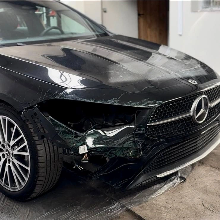 Czarny Mercedes z uszkodzonym przodem po kolizji, pęknięty zderzak i reflektor.